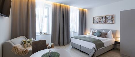 Ein modernes Hotelzimmer mit Bett, Sofa, Esstisch und Fernseher.