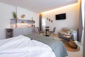 Ein modernes Hotelzimmer mit einem Bett, einer kleinen Küchenzeile, einem Essbereich und einer Sitzecke.