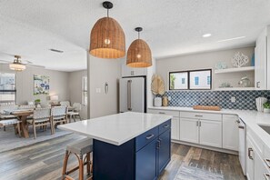 A modern kitchen with a central island, pendant lighting, and a dining area with a table and chairs. - 30A Dogwood Bungalow | Walk to Beach | Pet Friendly (Santa Rosa Beach)
