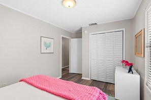 A bedroom with a bed, a white bedside table, a pink blanket, a white closet, and a framed picture on the wall. - 30A Dogwood Bungalow | Walk to Beach | Pet Friendly (Santa Rosa Beach)