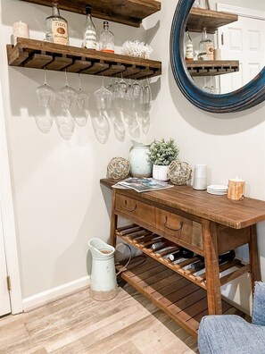 A wooden wine rack with bottles and glasses, a mirror, and a small table with decorative items. - 🏖️Front Porch Sitting | Private Pool, Spa & Screened Porch | Near Beach (Rosemary Beach)