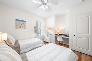 Ein Schlafzimmer mit zwei Betten, einem Schreibtisch, einem Stuhl, einem Deckenventilator und einem Fenster mit Jalousien.