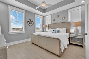 Ein Schlafzimmer mit einem großen Bett, zwei Nachttischen, einem Deckenventilator und Blick ins Freie.