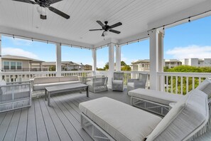 A covered outdoor deck with white railings, multiple seating areas including sofas and chairs, ceiling fans, and a view of neighboring houses. - ⭐Palms By The Sea | Rooftop Deck | 12,000 Sq Ft Pool | Beach Access⭐ (Seacrest Beach)
