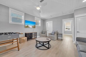 Ein Zimmer mit einem Kicker, einem runden Couchtisch, zwei gestreiften Sesseln, einem Sofa und einem an der Wand befestigten Fernseher.