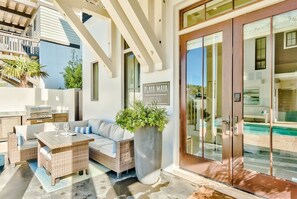 A modern outdoor living area with a wicker sofa, a wooden table, and a large planter. - Playa Maya | Pool | Steps to Rosemary | Sleeps 10 (Inlet Beach)