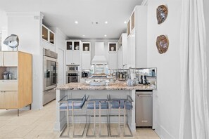 A modern kitchen with white cabinetry, a central island, and bar stools. - Playa Maya | Pool | Steps to Rosemary | Sleeps 10 (Inlet Beach)