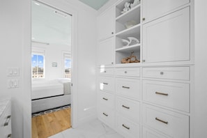 A white room with a bed, a wooden floor, and a white wardrobe with multiple drawers and shelves. - Playa Maya | Pool | Steps to Rosemary | Sleeps 10 (Inlet Beach)