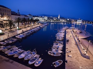 Uma marina com vários barcos atracados, um calçadão e edifícios ao fundo.