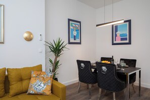 A dining area with a table set for two, two black chairs with decorative metal details, a potted plant, and framed artwork on the walls. - Luxury apartment with patio in the heart of Split (Split)