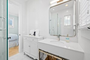 Een moderne badkamer met een glazen douchedeur, een wit wastafelmeubel en een grote spiegel.