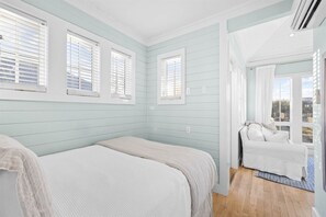 Een slaapkamer met een bed, een zithoek met een bank en een raam met zonwering.