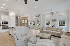 A modern kitchen with white cabinetry, a central island, and a dining area with a chandelier. - Recovery Room | Steps from The Big Chill | Private Deck, Pools & Bikes (Inlet Beach)
