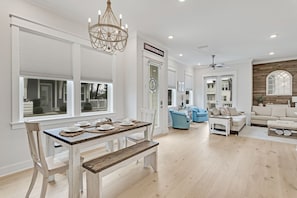 A spacious living room with a dining area, a chandelier, and a view of the outside. - Recovery Room | Steps from The Big Chill | Private Deck, Pools & Bikes (Inlet Beach)