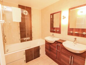 Ein modernes Badezimmer mit einer Badewanne, zwei Waschbecken, einem Waschtisch mit Schränken, einem Spiegel und einem Handtuchhalter.