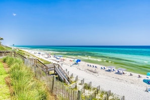 A beach with a wooden boardwalk, beach chairs, umbrellas, and a clear view of the ocean. - Sandy Knickers | Pool | Gulf Views | Beach Access (Seacrest)