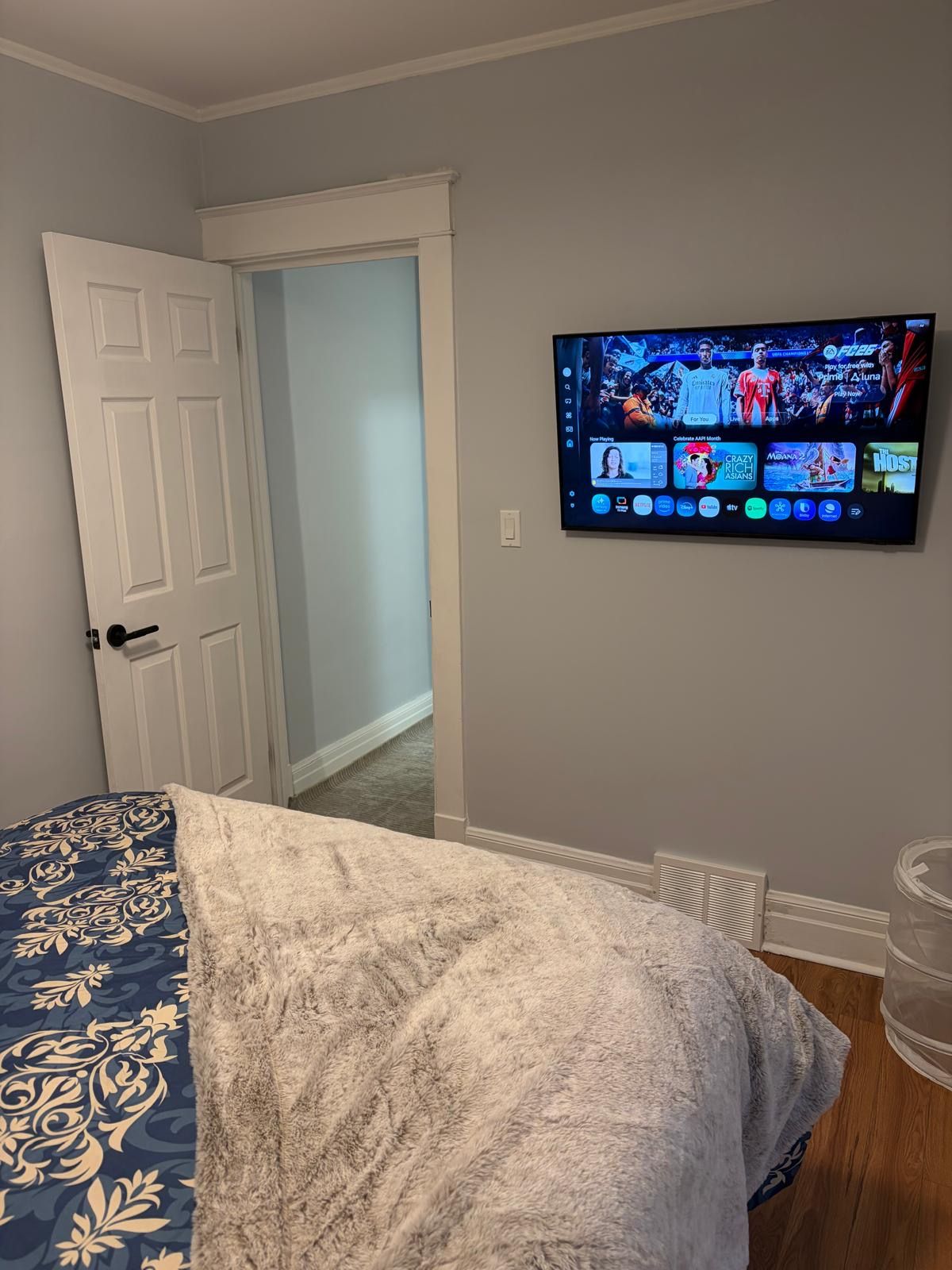 A bedroom with a bed, a television mounted on the wall displaying a sports channel, and a door leading to another room.