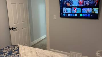 A bedroom with a bed, a television mounted on the wall displaying a sports channel, and a door leading to another room.