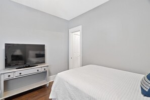 A bedroom with a television on a white stand, a white bed, and a door leading to another room. - Sea Sanctuary | Pool | 3 Balconies | Near Beach (Seacrest Beach)