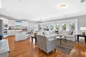 A spacious living area with a large sofa, a patterned armchair, and a coffee table. A kitchen with white cabinets and a dining area with a table and chairs are visible. - Sea Sanctuary | Pool | 3 Balconies | Near Beach (Seacrest Beach)
