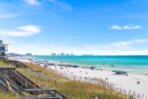 Ein Strand mit einer Holzpromenade, Strandsonnenschirmen und einer Stadtansicht in der Ferne.