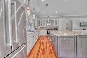 A kitchen with a stainless steel refrigerator, wooden flooring, white cabinetry, and pendant lighting. - 🌊Second Wind | Screened Porch | 4 Bikes 🚲 | Sleeps 8 (Santa Rosa Beach)