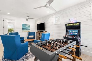 Ein Raum mit einem Kicker, blauen Stühlen, einem Fernseher und einem Deckenventilator.