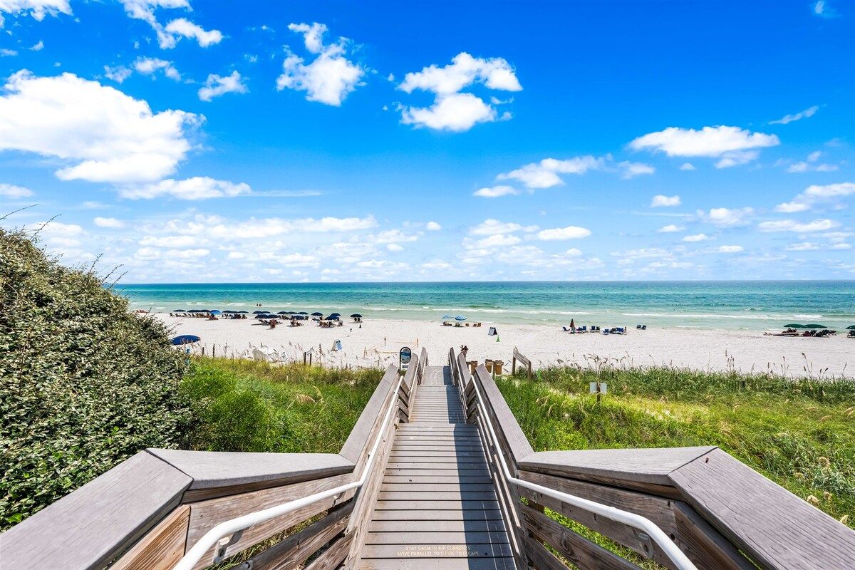 A wooden boardwalk leading to a beach with clear skies and a calm sea.
