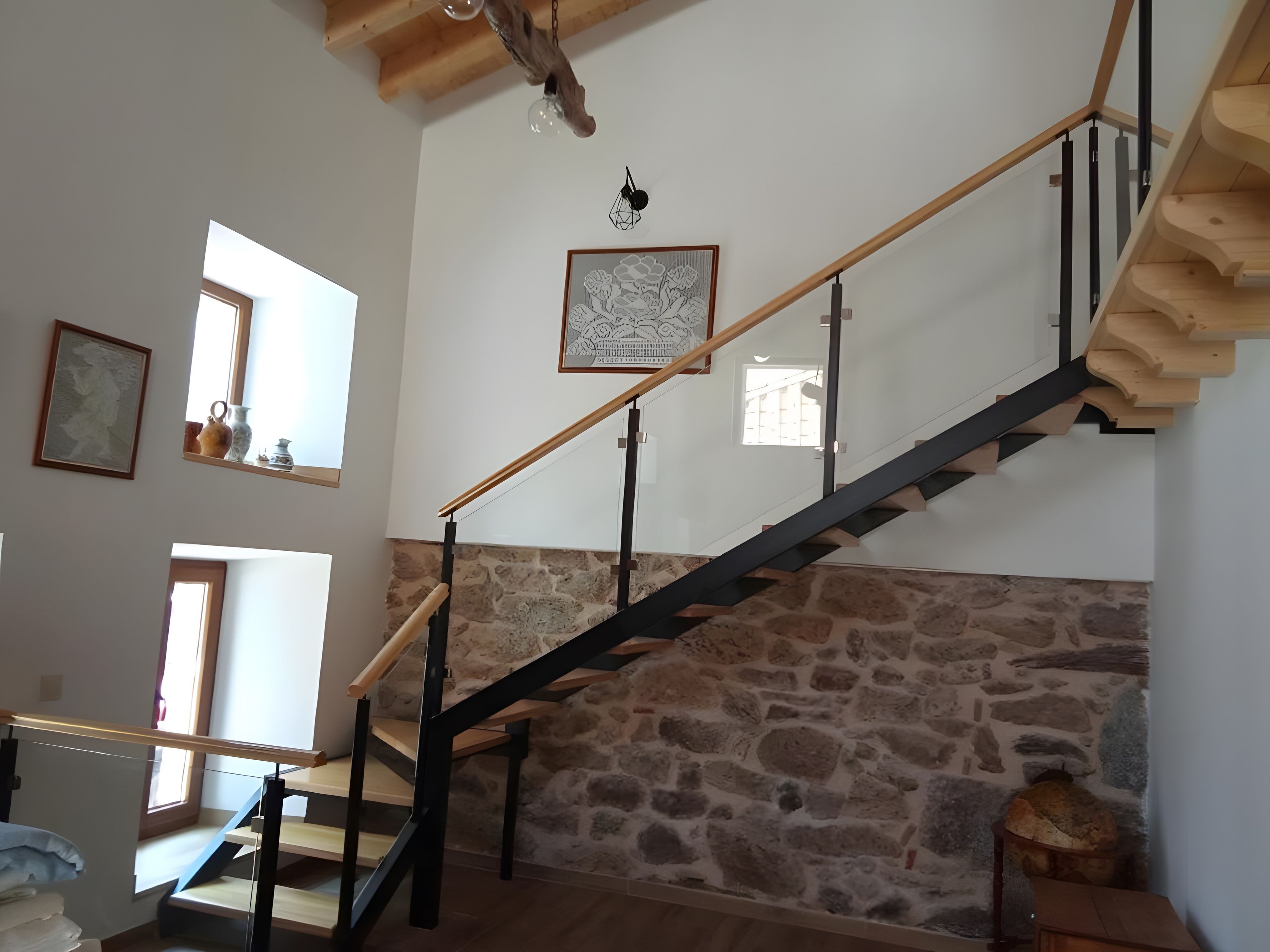Un escalier avec un mur en pierre, des rampes en bois et un luminaire suspendu.
