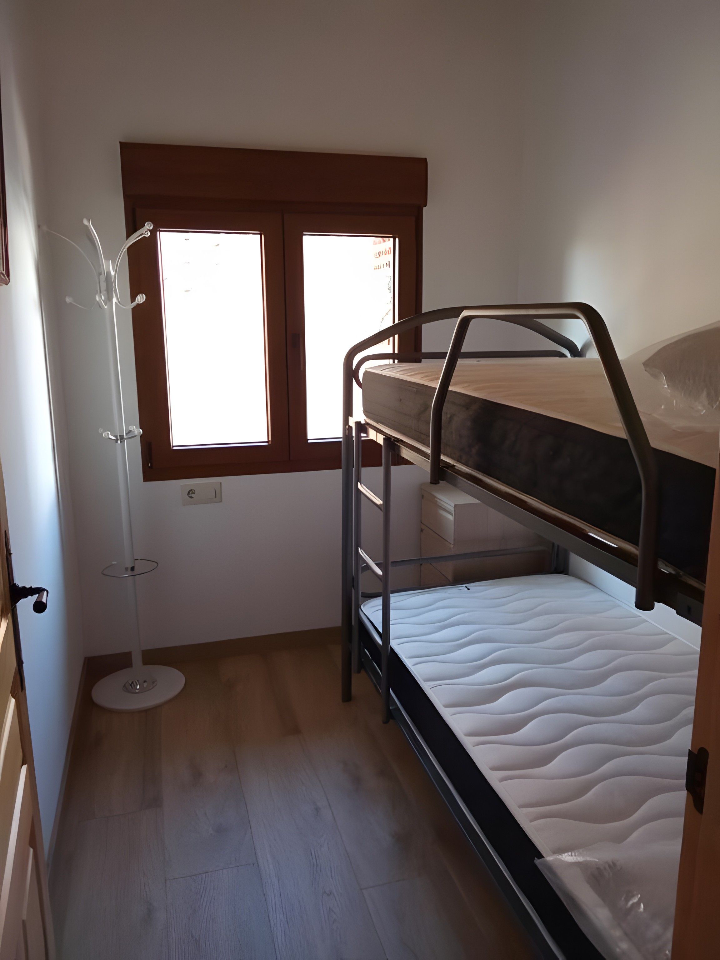 A bunk bed room with a window, a coat rack, and a bedside table.