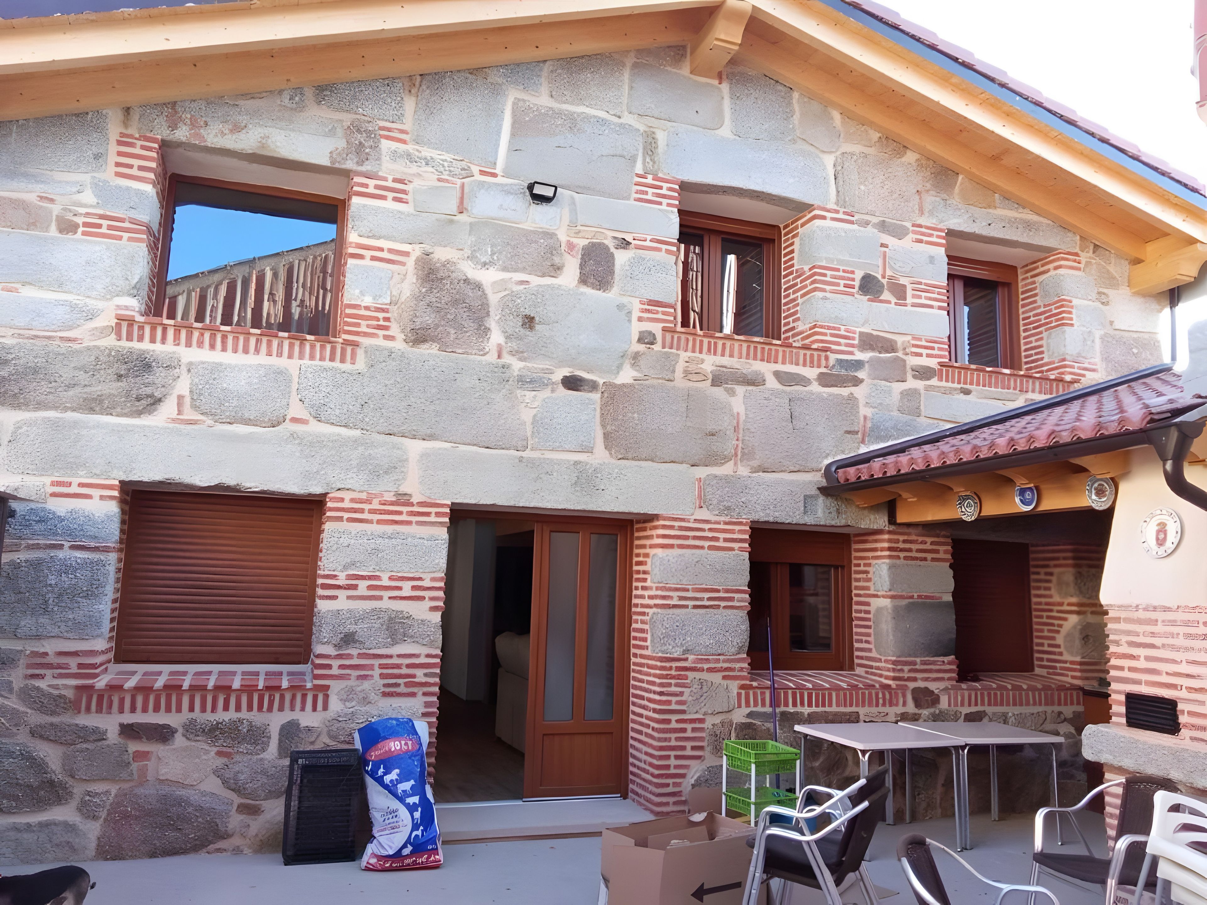 A stone building with multiple windows and a balcony, a table, chairs, and a bag of feed.