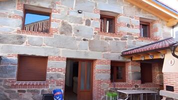 A stone building with multiple windows and a balcony, a table, chairs, and a bag of feed.