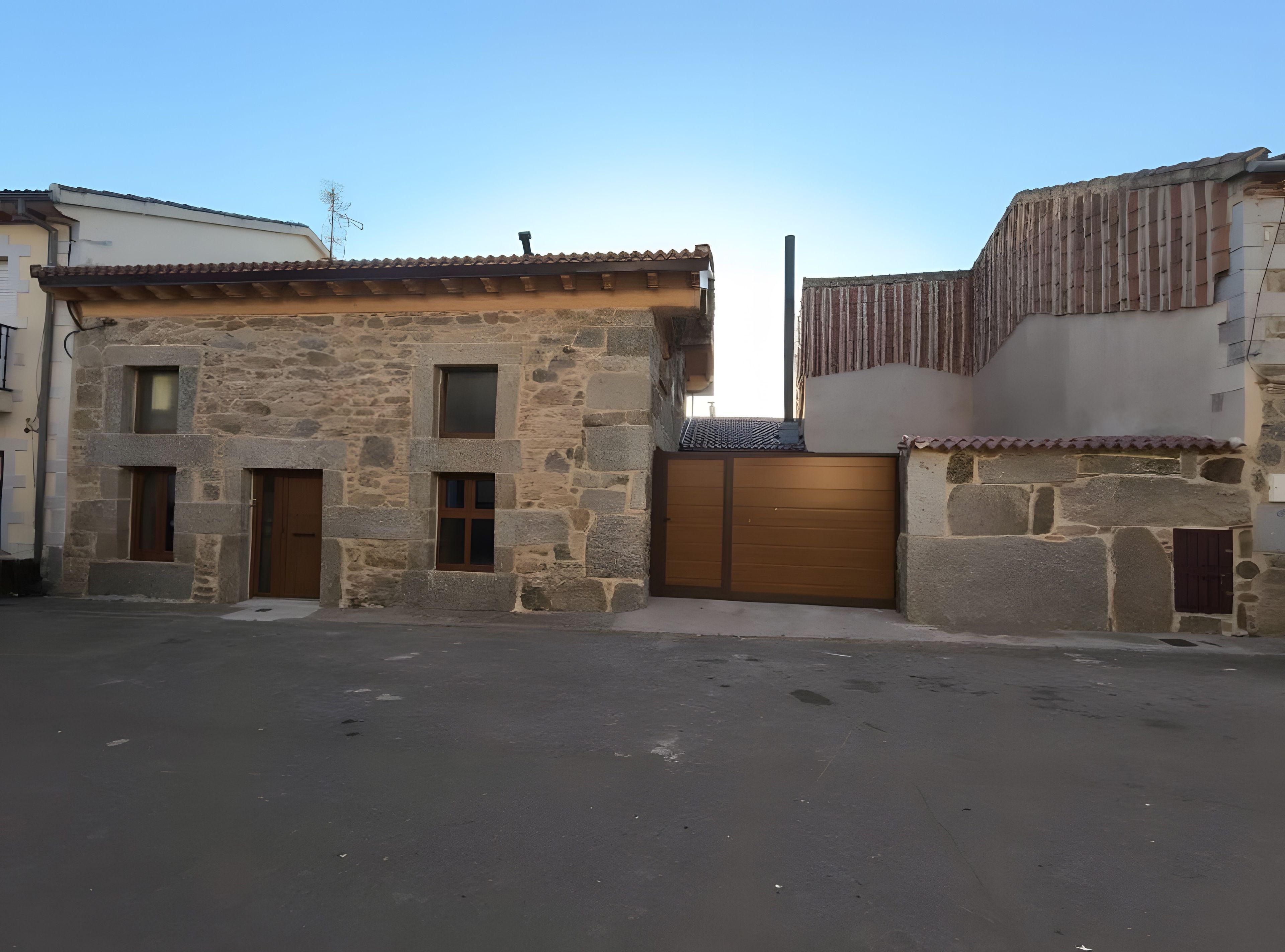 Un edificio de piedra con techo de tejas, puerta de madera y entrada protegida por una reja.