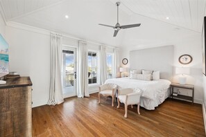 Een slaapkamer met een groot bed, twee stoelen, een nachtkastje, een plafondventilator en uitzicht op de omgeving.