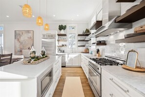 Een moderne keuken met witte kasten, roestvrijstalen apparatuur en hanglampen.