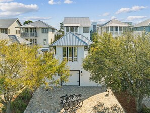 A row of white buildings with blue roofs, a paved courtyard, and bicycles parked in front. - Stepping Stone Main House | Pool | Steps from Rosemary Beach (Inlet Beach)