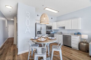 Een moderne keuken met witte kastjes, een eettafel voor vier personen en een hanglamp.