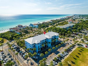 A coastal hotel with a parking lot, surrounded by palm trees and a view of the ocean. - ☀️Sun Stone | Steps from Beach | Pool | Sleeps 6☀️ (Santa Rosa Beach)