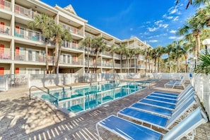 Een hotel met een zwembad, meerdere balkons en palmbomen.