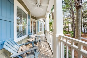A covered porch with two Adirondack chairs, a ceiling fan, and a stone-tiled floor. - Sunshine Shack | Steps to Rosemary | Pool | Sleeps 12 (Seacrest Beach)