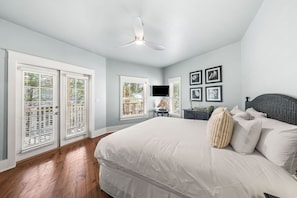 A bedroom with a large bed, a ceiling fan, and a TV on the wall. - Sunshine Shack | Steps to Rosemary | Pool | Sleeps 12 (Seacrest Beach)