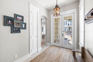 A hallway with a patterned rug, a door with glass panels, and a hanging light fixture. - Sunshine Shack | Steps to Rosemary | Pool | Sleeps 12 (Seacrest Beach)