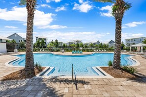 Ein Pool mit Liegestühlen und Palmen, umgeben von Gebäuden.