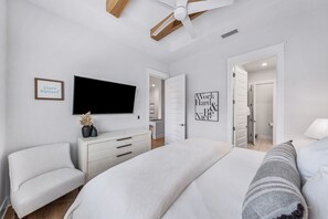 Ein Schlafzimmer mit einem Bett, einem Fernseher, einer Kommode, einem Sessel und einer Tür zu einem Badezimmer.
