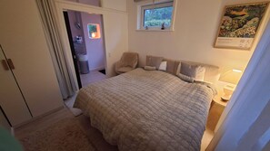 A bedroom with a bed, a chair, a nightstand, a window, and a painting on the wall.