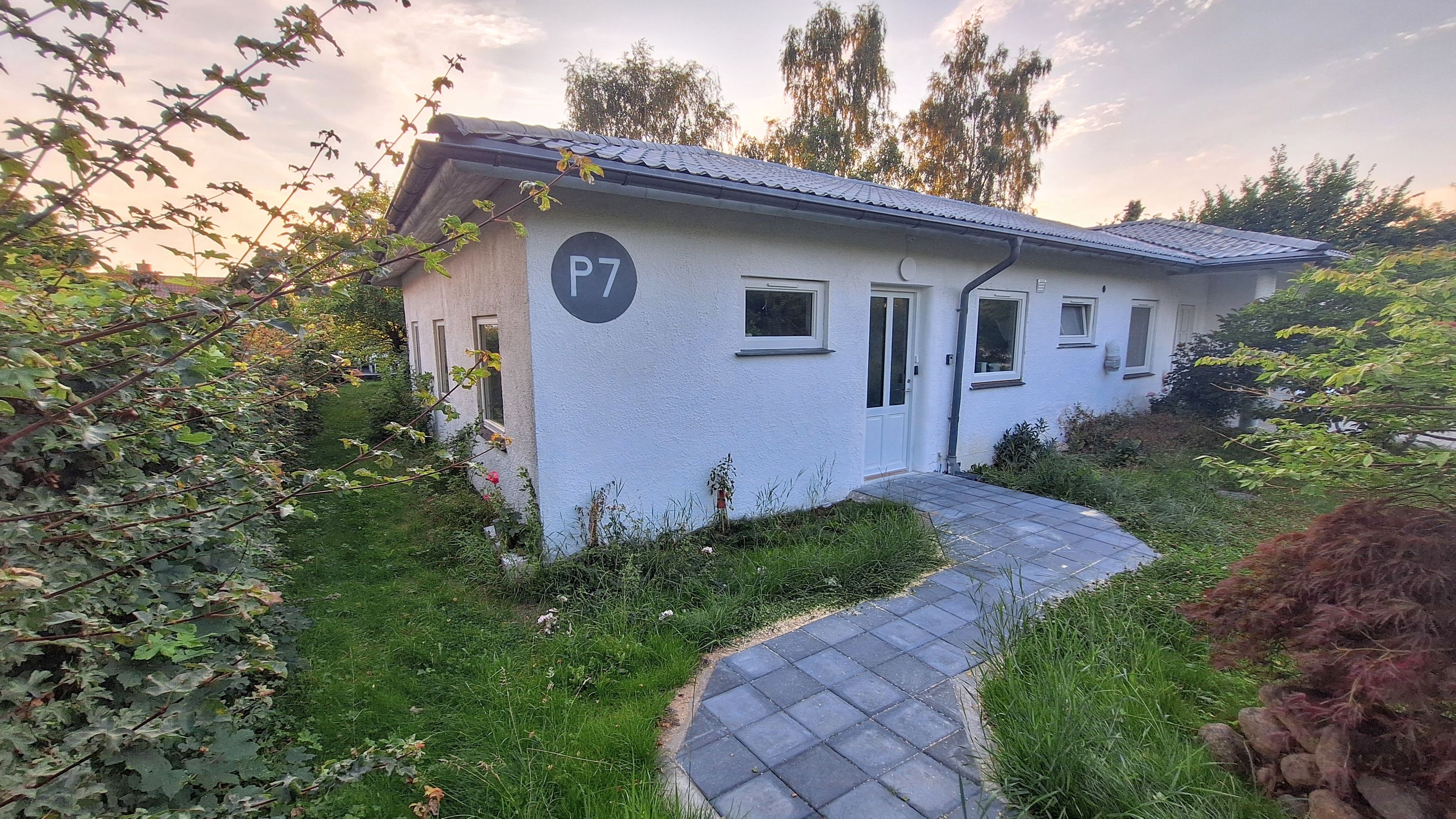 Un edificio a un piano con facciata bianca, vialetto lastricato e un piccolo giardino.