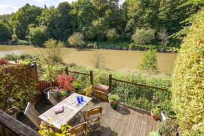 A deck with a table and chairs overlooking a river, surrounded by greenery. - Townhouse on the River, Decking & Private Parking (Bristol City)