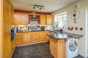 Une cuisine avec des meubles de rangement en bois, un lave-linge encastré et une horloge au mur.