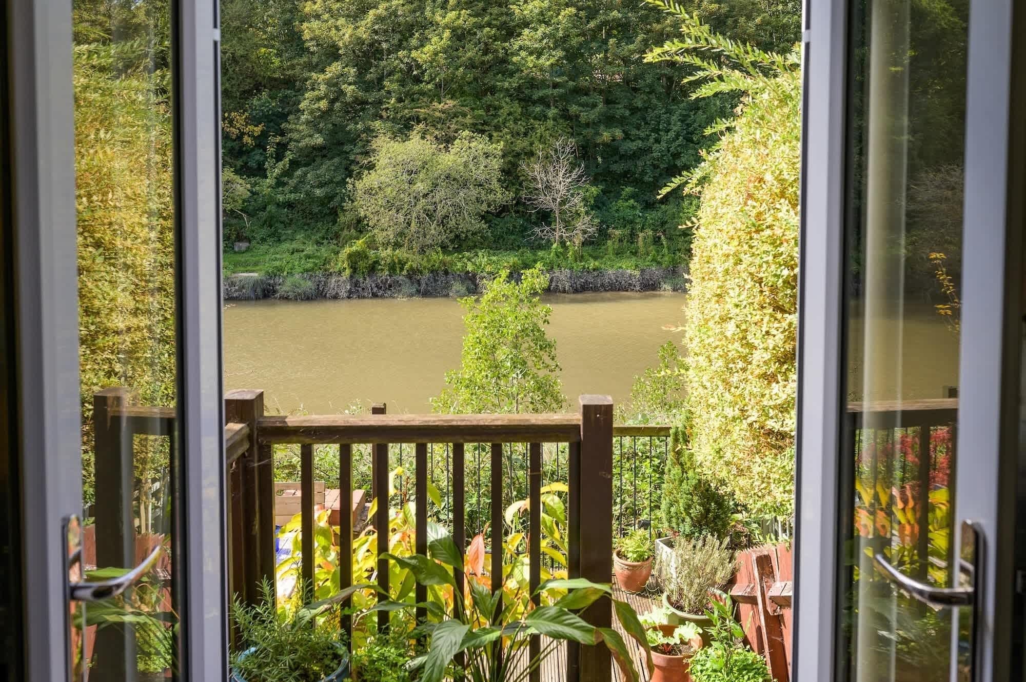 A view from a balcony with a wooden railing, overlooking a river and a dense green landscape.