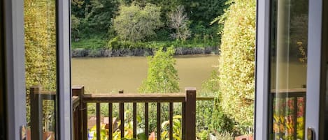 Une vue depuis un balcon doté d’une balustrade en bois, donnant sur une rivière et un paysage verdoyant et luxuriant.